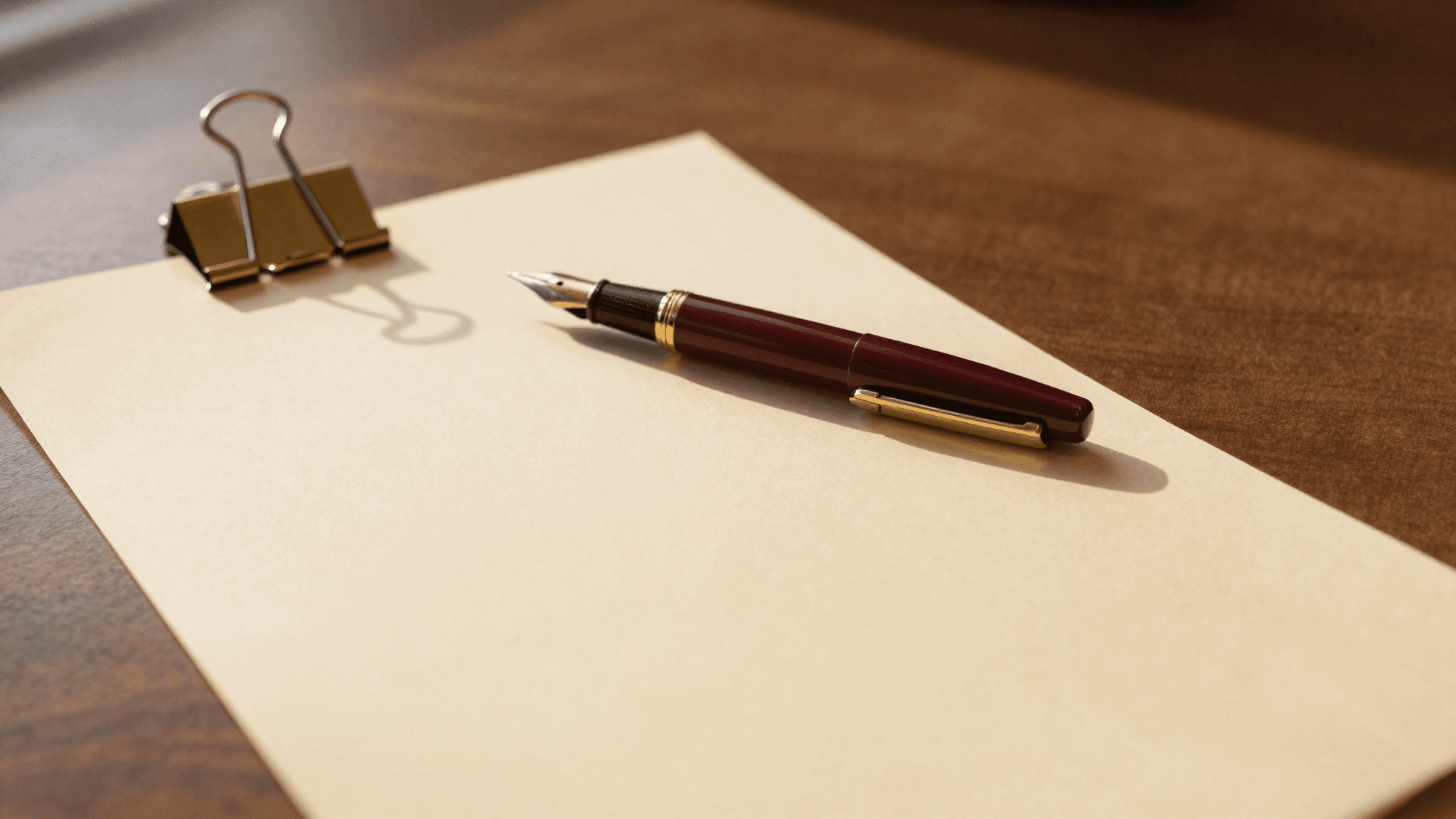 A marked-up contract on a walnut desk anchored by a brass paper clip, smaller pages stacked beside it
